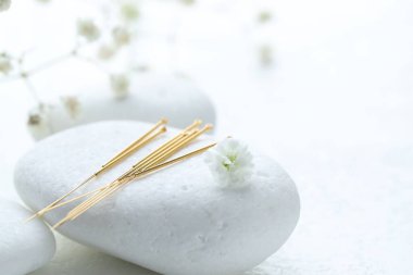 Akupunktur iğneleri, çakıl taşları ve çiçek tomurcukları beyaz desenli masada, yakın plan. Metin için boşluk