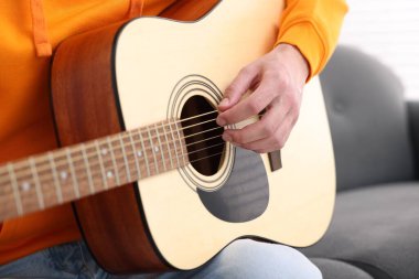 Genç adam kanepede gitar çalıyor, yakın plan.