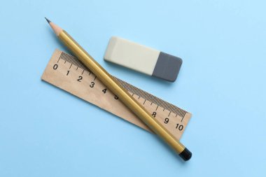 Açık mavi arkaplanda silgi, kalem ve cetvel, üst görünüm