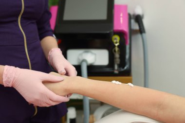 Profesyonel kozmetik uzmanı müşterinin koluna nemlendirici losyon sürüyor. Güzellik salonundaki tüy dökümü prosedüründen sonra, yakın plan.