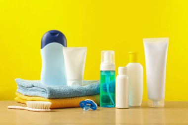 Baby cosmetic products and bath accessories on wooden table against yellow background