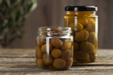 Ahşap masada cam kavanozlarda turşulu zeytin, yakın plan.