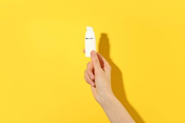 Sarı arka planda serum şişesi olan kadın, yakın plan. Vücut bakımı ürünü
