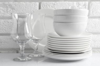 Different clean dishware on white table near brick wall