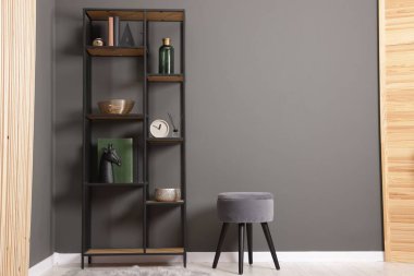 Shelving unit with decor, stool and folding screen near grey wall indoors