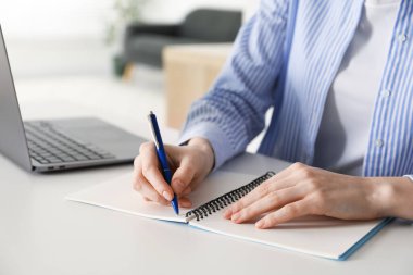 Beyaz masada dizüstü bilgisayarın yanında notlar alan bir kadın, yakın plan. Kendi kendine çalışma.