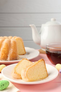 Lezzetli kek parçaları, pembe ahşap masada paskalya yumurtası ve çay.