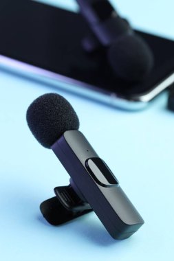 Açık mavi arkaplanda kablosuz alıcısı olan Lavalier mikrofonlar ve akıllı telefon, seçici odak
