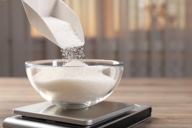 İçerideki ahşap masada dijital mutfak terazisine şeker koymak, yakın plan. Metin için boşluk