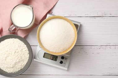 Dijital mutfak terazisi, bir kase şeker ve beyaz ahşap masa üzerindeki diğer ürünler, düz yatak. Metin için boşluk