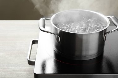 Kaynar suyla pişirme tenceresi ve ahşap masa üzerinde gri arka plan, yakın çekim