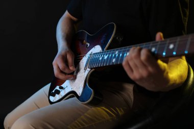 Siyah arka planda arabulucuyla gitar çalan adam, ele odaklan