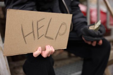 Evsiz adam kelime işareti tutuyor Yardım ve para açık havada, seçici odaklanma
