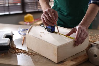 İçerideki masada bant ve kalemle ahşap kutuyu ölçen adam, yakın plan.