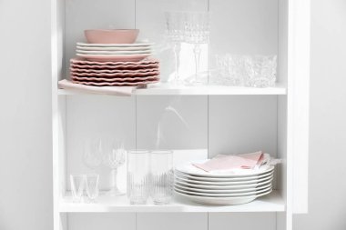 Beyaz duvarın yanındaki raflarda temiz bardaklar ve tabaklar.