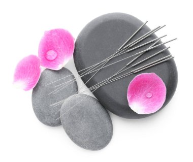 Akupunktur iğneleri, spa taşları ve yaprakları beyaza izole edilmiş.