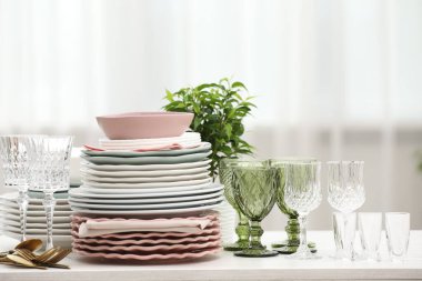 Temiz bardaklar, tabaklar, çatal bıçak takımı ve yeşil saksı.