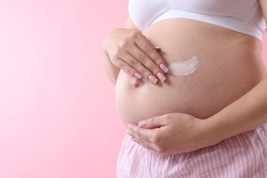 Karnında krem olan hamile kadın pembe arka planda, yakın plan. Metin için boşluk