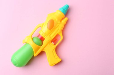 Açık pembe arka planda parlak plastik su tabancası, üst manzara. Metin için boşluk