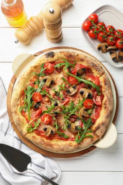 Mantarlı, domatesli, roka ve beyaz ahşap masada servis edilen lezzetli bir pizza.