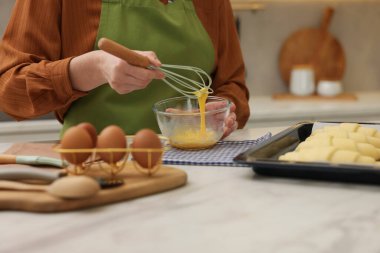 Mutfaktaki beyaz mermer masada, çiğ kruvasan yanında yumurta yıkayan bir kadın.