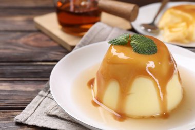 Karamel soslu lezzetli puding ve ahşap masada nane şekeri, yakın plan.