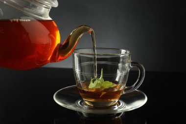 Çaydanlıktan taze demlenmiş çayı siyah masaya, cam fincana dökerek.