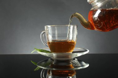 Koyu ayna masasında çaydanlıktan fincana taze demlenmiş çay dökülüyor.