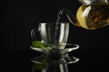 Koyu ayna masasında çaydanlıktan fincana taze demlenmiş çay dökülüyor.