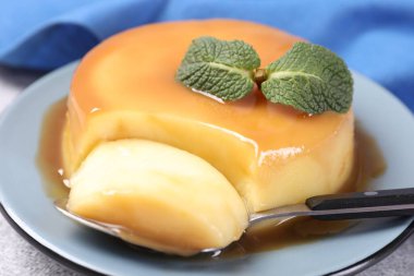 Karamel soslu lezzetli puding, gri masada nane ve kaşık, yakın plan.