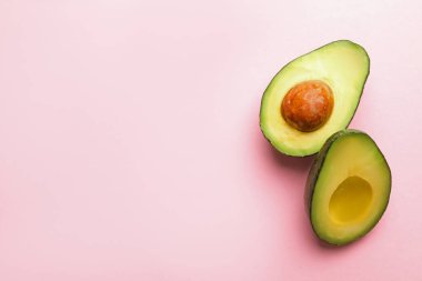 Pembe arka planda taze avokado yarıları, düz yatış. Metin için boşluk