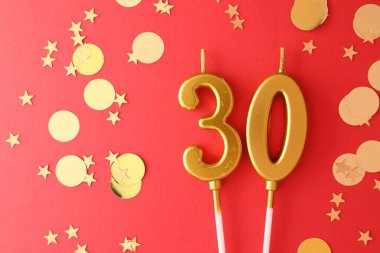 30th birthday. Number shaped candles and confetti on red background, flat lay