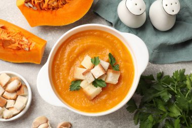 Lezzetli balkabağı kremalı çorba, kızarmış ekmek ve yeşil desenli masada maydanoz.