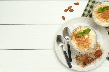 Tarçınlı, naneli, bademli ve beyaz ahşap masadaki kaşıklı leziz sütlaç. Metin için boşluk