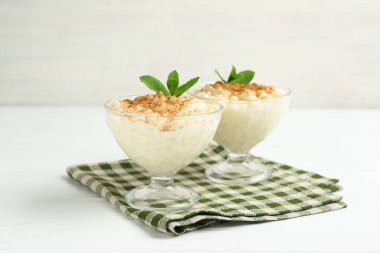 Tarçınlı lezzetli pirinç pudingi ve beyaz ahşap masadaki cam tatlı kaseleri, yakın plan.