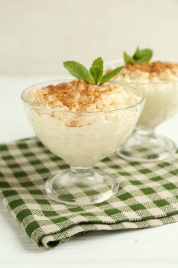 Tarçınlı lezzetli pirinç pudingi ve beyaz ahşap masadaki cam tatlı kaseleri, yakın plan.