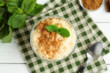 Tarçınlı lezzetli pirinç pudingi, beyaz ahşap masada nane ve kaşık, düz uzanmış