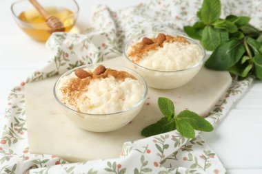 Tarçınlı lezzetli sütlaç, badem, bal ve naneli beyaz ahşap masa, yakın plan.