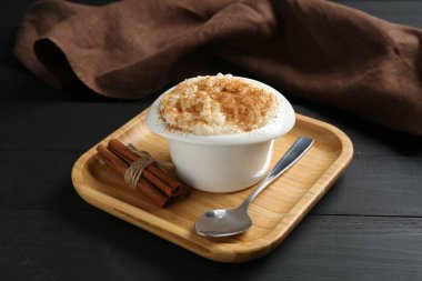 Tarçınlı lezzetli sütlaç ve siyah ahşap masada kaşık, yakın plan.