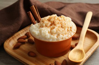 Tarçınlı lezzetli sütlaç, badem ve kaşık ahşap masada, yakın plan.