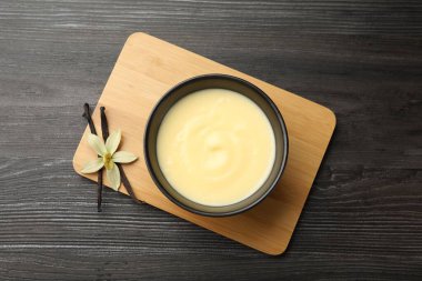 Lezzetli vanilyalı puding kasede, çiçek ve kapsüller ahşap masada, üst manzara