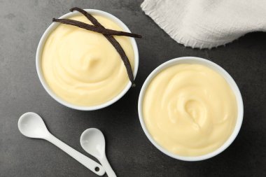 Lezzetli vanilyalı puding, kapsüller ve kaşıklar siyah masada, düz yerde.