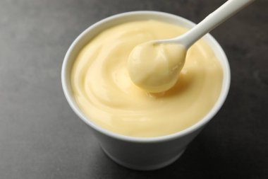 Siyah masadaki kaşıklı lezzetli vanilyalı puding, yakın plan.