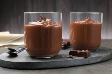 Lezzetli puding ve çikolata parçaları gri masada, yakın plan.