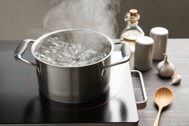 Kaynar suyla pişirme tenceresi ve ahşap masa üzerinde gri arka plan, yakın çekim