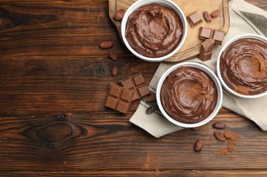 Tabaklardaki lezzetli pudingler, çikolata parçaları ve kakao çekirdekleri ahşap masada, düz bir şekilde. Metin için boşluk