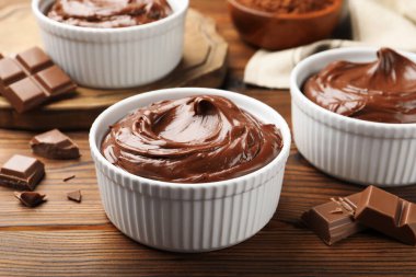 Tabaklardaki lezzetli pudingler ve ahşap masadaki çikolata parçaları, yakın plan.