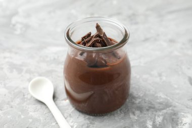 Cam kavanozda çikolatalı puding ve açık gri masada kaşık, yakın plan.