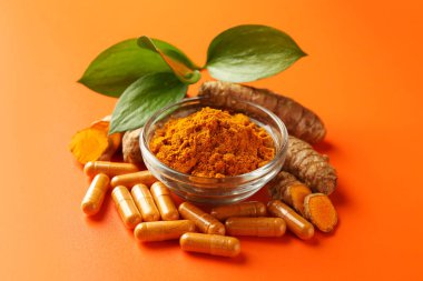 Kavanozda zerdeçal tozu, turuncu arka planda kök ve kapsüller, yakın plan.