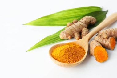 Kaşıkta zerdeçal tozu, beyaz arka planda yeşil yapraklar ve kökler, yakın plan. Metin için boşluk